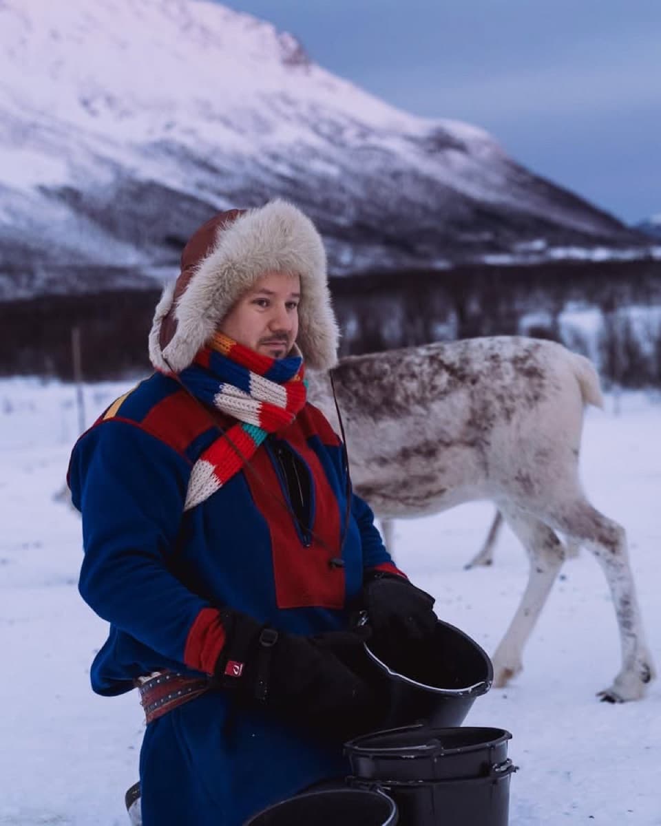 Jon Mikkel in traditional Sami gákti feeding reindeer in Arctic winter