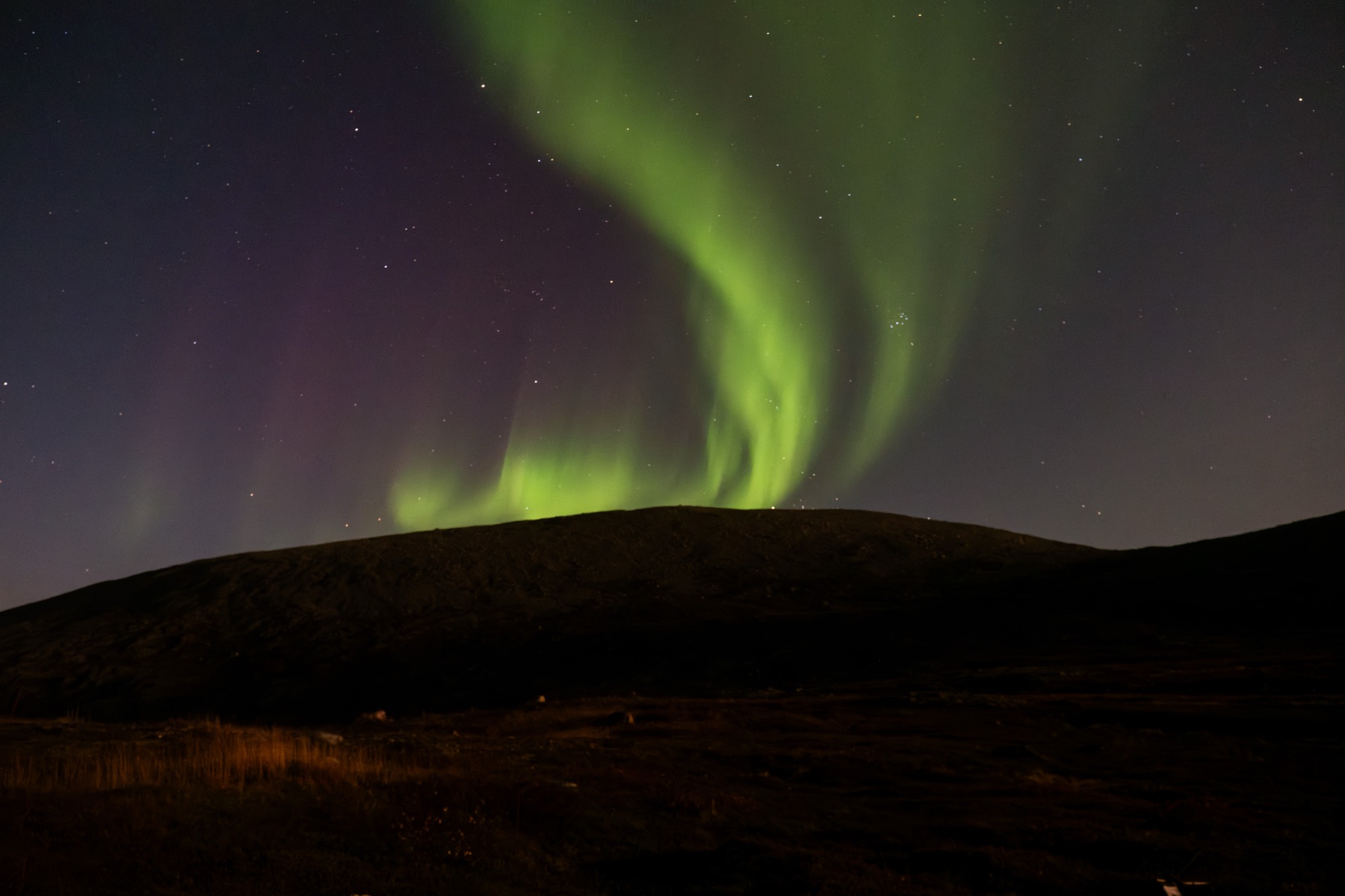 A green aurora arc over a dark ridge
